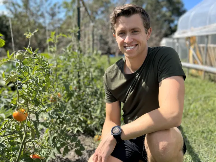 Ryan, founder of Urban Permascapes, kneeling beside tomato plants at an urban farm